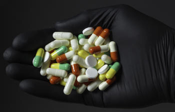 Pills and capsules of several colors in a hand on a gray background.