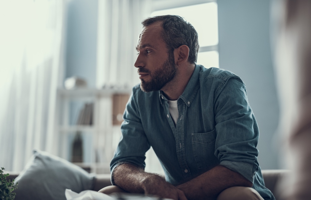 calm bearded middle aged man sitting at home and thoughtfully looking into the distance